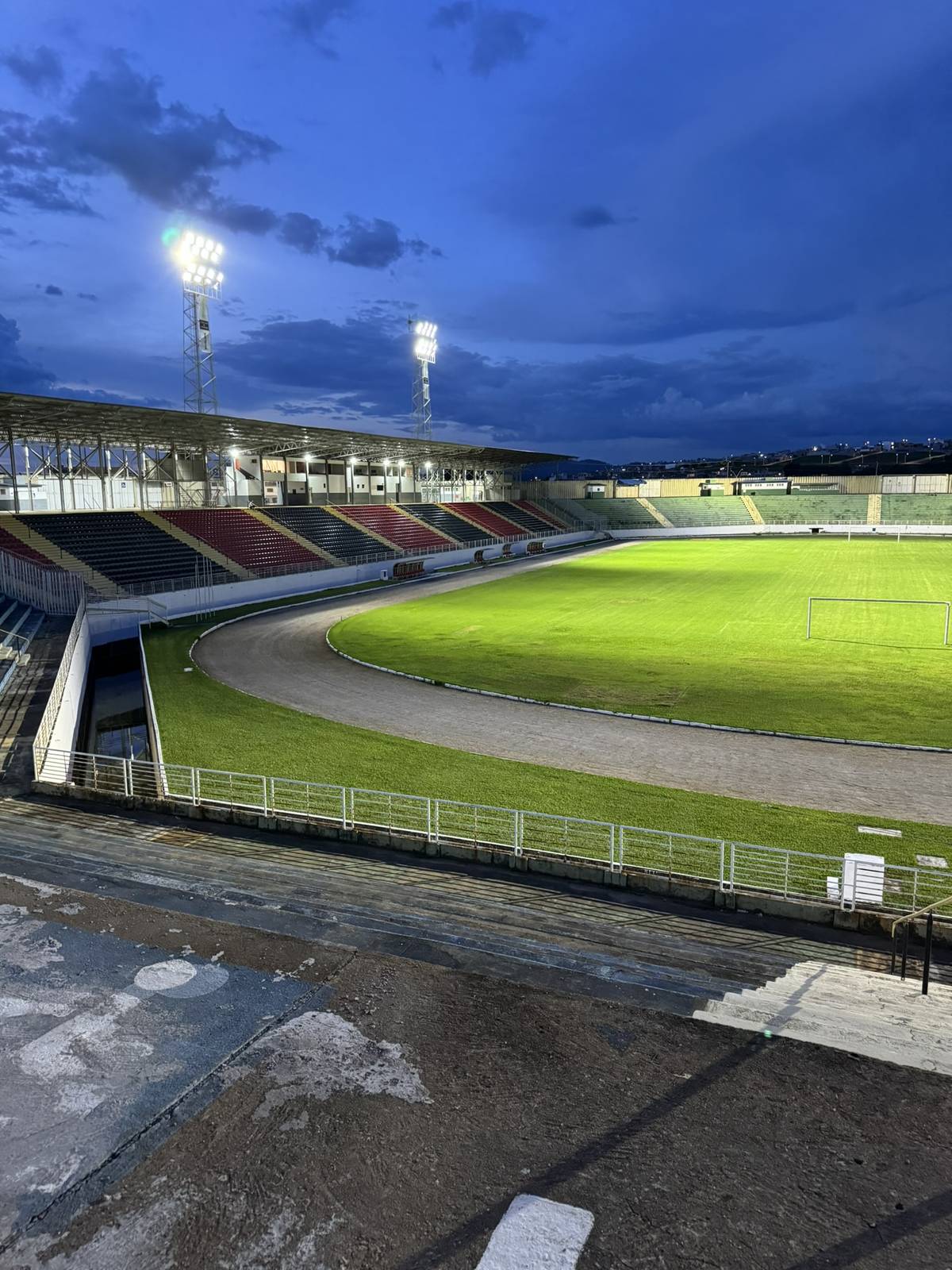 Estádio de futebol com pista de atletismo ao entardecer, iluminado por torres de refletores LED